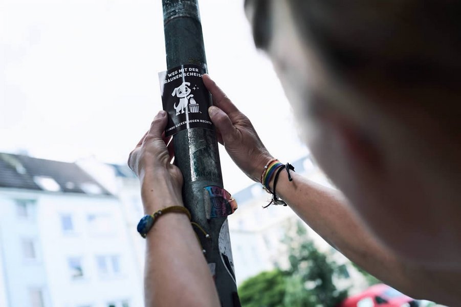 Ein Sticker wird an einen Pfeiler mit vielen anderen Stickern geklebt